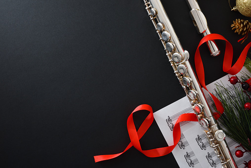 Background with metal flute on black table with Christmas decoration and sheet music. Top view.