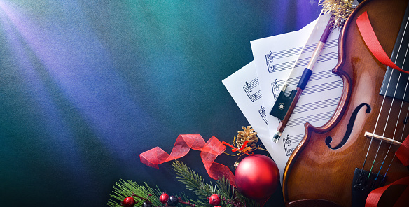 Christmas musical event concept background with violin on black table with sheet music, Christmas decoration and colored lights. Top view.