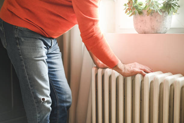 mature adult man sits and warms himself by the radiator in the room mature adult man sits and warms himself by the radiator in the room warms stock pictures, royalty-free photos & images