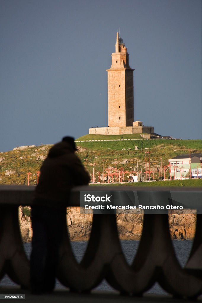Torre de Hércules ancient lighthouse, unrecognizable person leaning on stone railing, looking at view. A Coruña city, Galicia, Spain. Torre de Hércules ancient lighthouse, unrecognizable person leaning on stone railing, looking at seascape view. A Coruña city, Galicia, Spain. A Coruna Stock Photo