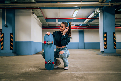 Cheerful teen skater girl with headphones in the public parking garage