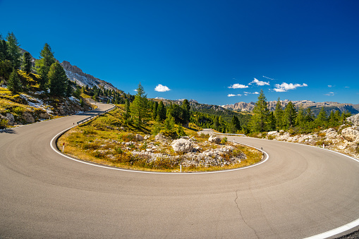 Empty curvy asphalt mountain pass road high up in the dolomites on sunny day with blue sky
