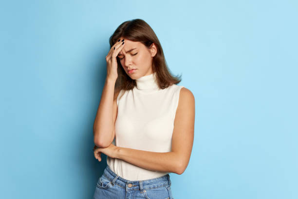 istock Portrait of young beautiful woman posing, touching head, suffering from headache isolated over blue studio background. Medical treatment 1442568708
