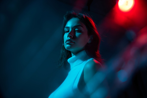 Portrait of young beautiful woman posing isolated over blue studio background in neon light. Nightclub lifestyle. Concept of youth culture, emotions, facial expression, fashion. Copy space for ad