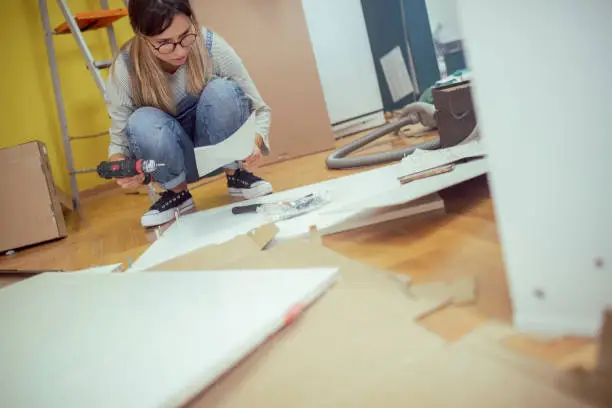 A woman reads the instructions for assembling the furniture and tries to assemble it herself