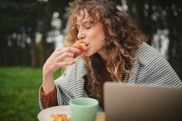 frau genießt es, ein croissant zu essen, während sie telearbeit macht und campt - woman eating croissant stock-fotos und bilder