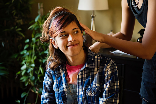 Transgender girl and non-binary teen friends doing their hair at home. Both are multiracial, one half asian, the other half latino. Horizontal indoors waist up shot with some copy space. This was taken in the suburbs of Montreal, Quebec, Canada.