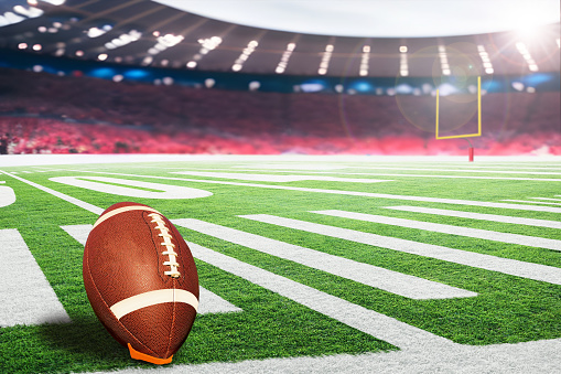 American football stadium with goal post and ball on tee ready for field goal kick. Focus on foreground ball with shallow depth of field on background and copy space.
