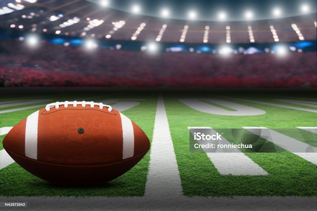 American football on field with dramatic spot lights on ball American football on field in stadium with dramatic spot lighting and copy space. Focus on foreground ball with shallow depth of field on background. College American Football Stock Photo