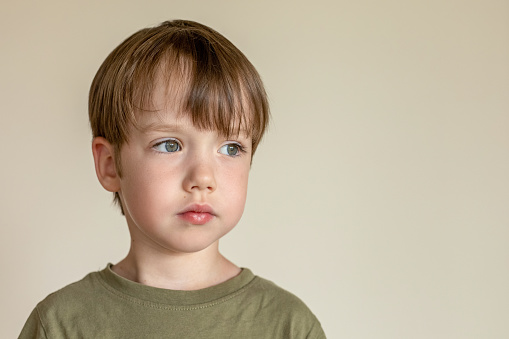 Indoor portrait of a 5 year old white boy with brown hair in a green t-shirt against a beige background