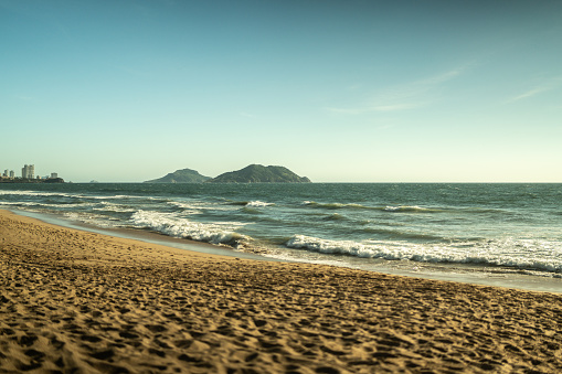 Tourists and locals enjoying the sun on famous Copacabana Beach in Rio de Janeiro. Merchandise in the form of beach towels and other goods is visible.