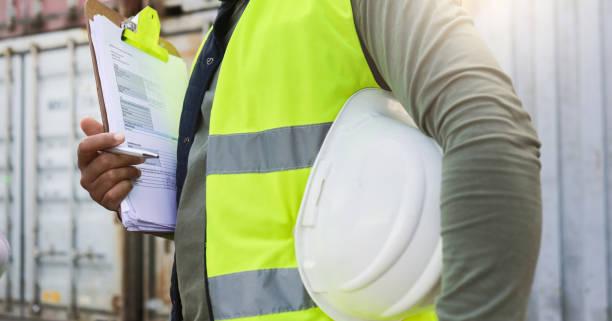 istock Man, checklist and work in logistics with helmet by container at port. Black man, notes and pen in hand to check stock while working in shipping, cargo and transportation industry in Cape Town 1442579025