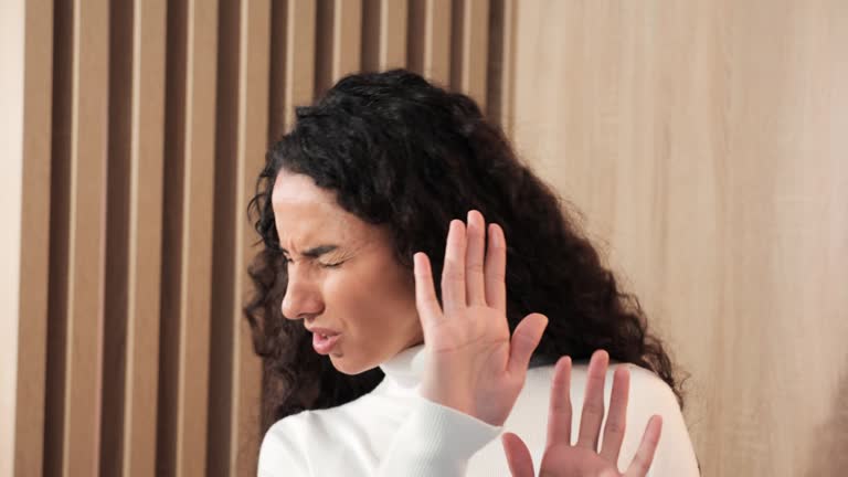 Don't do that, I'm scared, stop it. The girl covers herself with her hand from the man's aggressive behavior at home. Displeased young brunette woman covering eyes and gesturing stop, problem.