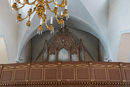 Estonia, Tallinn - July 21, 2022: Inside St. Peter and St. Paul Cathedral. Organ on its loft above entrance. Silver pipes set in sculpted dark wood against white ceiling. Golden chandelier,