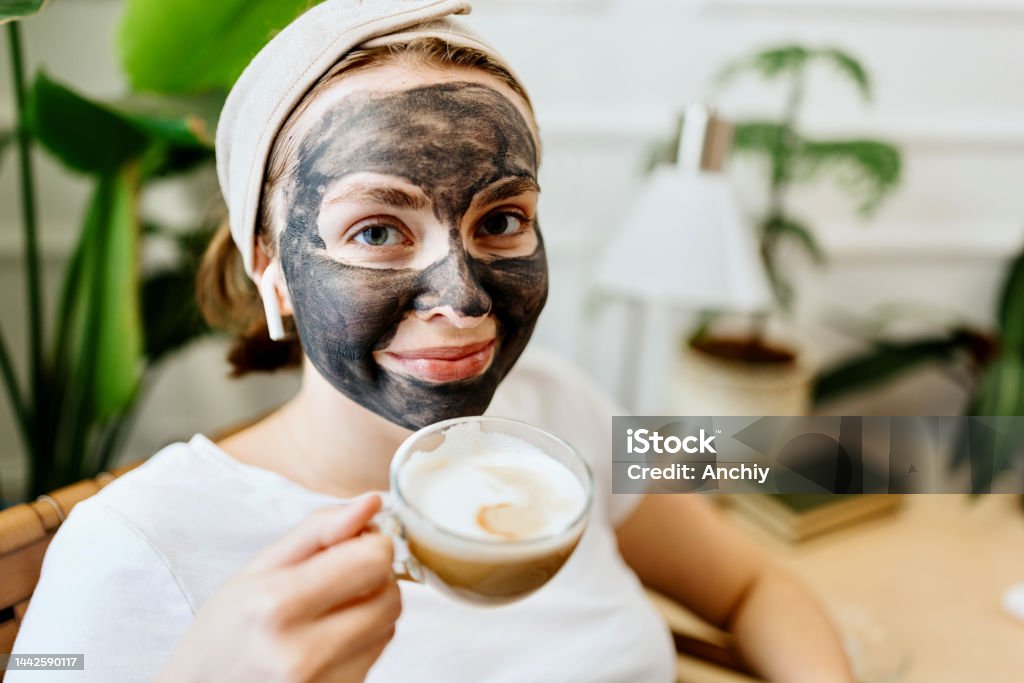 Young woman enjoying her cup of coffee Woman with Charcoal Facial Cleansing Mask relaxing at home with cup of coffee 20-24 Years Stock Photo
