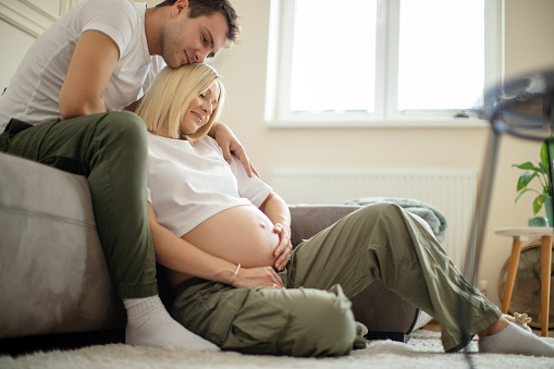 Beautiful pregnant woman and her husband sitting on floor and relaxing together. They are very happy and enjoying their love a lot.