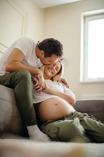 Beautiful pregnant woman and her husband sitting on floor and relaxing together. They are very happy and enjoying their love a lot.