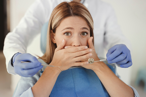 Woman at dental practice refusing dentist treatment with her hand in front of the mouth