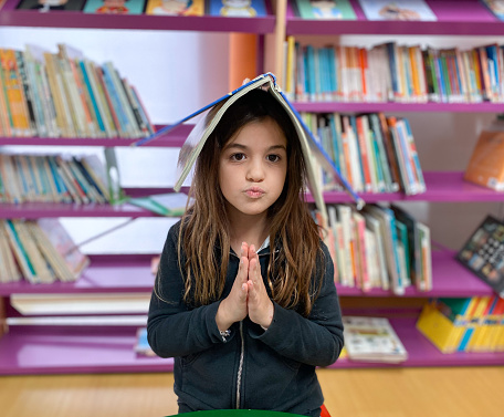 Girl sitting in the library praying with a book on her head