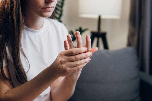 jovem doente com artrite e dor nas articulações nos dedos sentados no sofá em casa. close-up da mão feminina com sintomas de gota crônica. cuidados de saúde fácil conceito de auto-massagem. dor nos dedos - sprain human joint palm human arm - fotografias e filmes do acervo