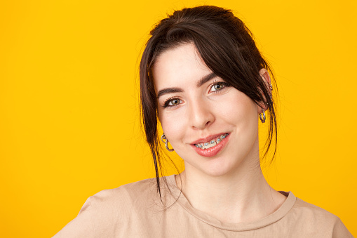 Close-up studio portrait of a cheerful 20 year old white woman with black hair in a beige t-shirt against a yellow background