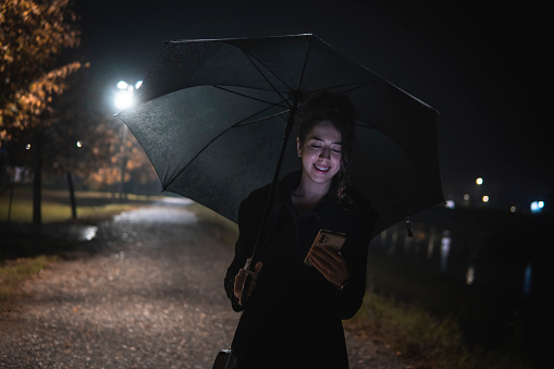 Image of a caucasian girl using the phone with an umbrella in her hand in the rain outside