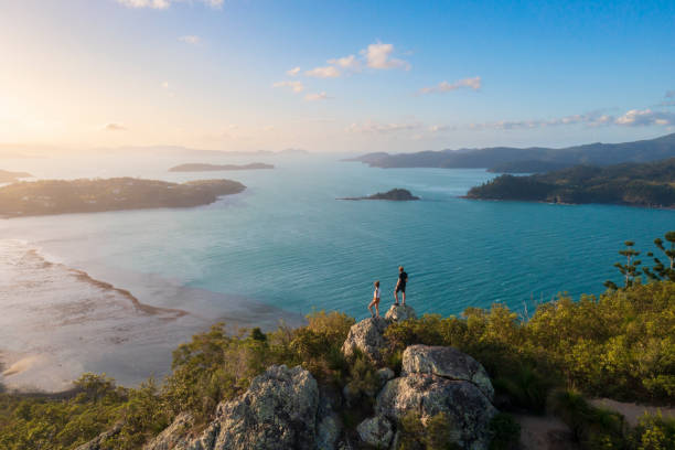 couple enjoying the view on top mountain overlooking whitsundays ocean - australië stockfoto's en -beelden