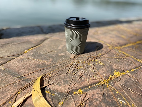 Plastic cup of hot coffee on walkside at sea background