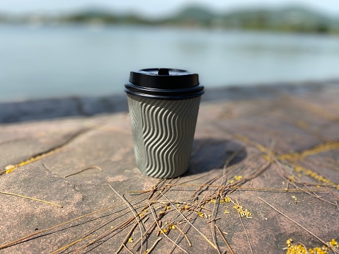Plastic cup of hot coffee on walkside at sea background