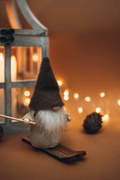 istock A cute dwarf, in a high hat, on skis and on a brown background, decorated with lanterns with a candle, cones and a garland. Suitable for postcards and Christmas greetings 1442618354