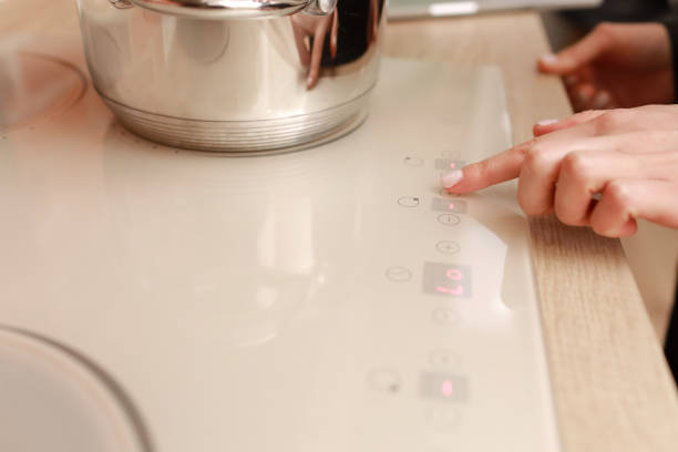 istock Female hand turns on electric hob closeup, finger presses sensor button on modern white induction cooker. Metal steel saucepan on kitchen stove top panel, modes of cooking surface, Domestic equipment 1442619452