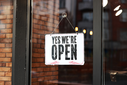 Inscription Yes we're open metal plate with black and white sign on glass door store, cafe, beautystore, barbershop after coronavirus lockdown quarantine. business reopen again.