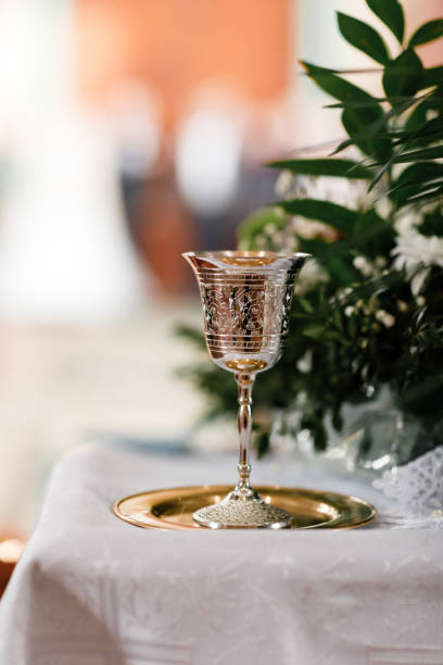 golden chalice with drawings on it for drinking wine for communion on the golden plate in church. Greens on background. copy space. selective focus golden chalice with drawings on it for drinking wine for communion on the golden plate in church. Greens on background. copy space. selective focus. crystal chalice stock pictures, royalty-free photos & images