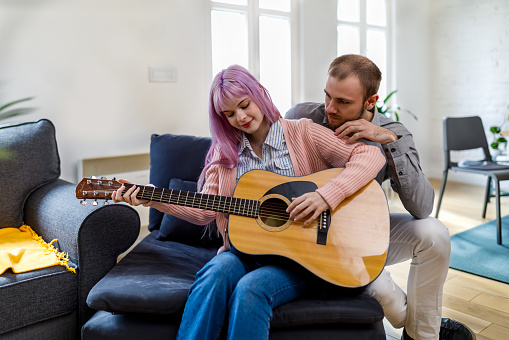 A young woman is playing the guitar while her boyfriend is enjoying the rhythm of the music. A happy couple is spending beautiful moments together to the sounds of a guitar.