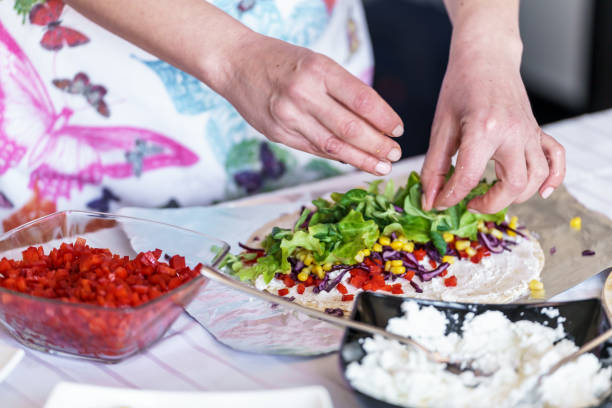 A woman is making tortillas filled with meat and vegetables.