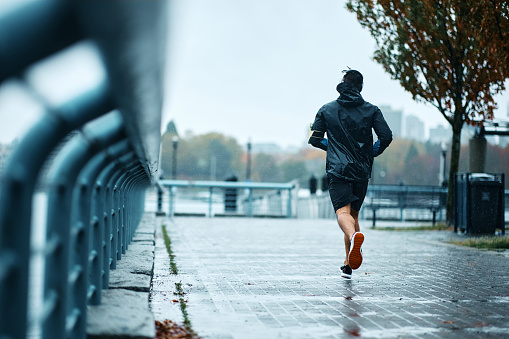 Back view of male athlete running on the street during rainy day. Copy space.