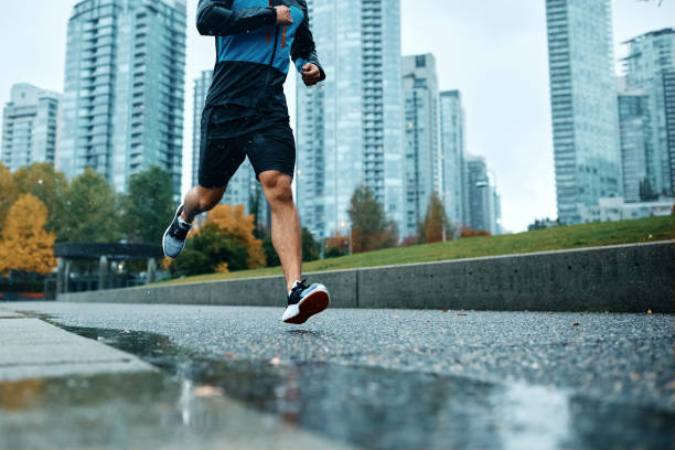 Unrecognizable athletic man running during rainy day. Below view of unrecognizable athlete jogging in the rain. Copy space. running shorts stock pictures, royalty-free photos & images