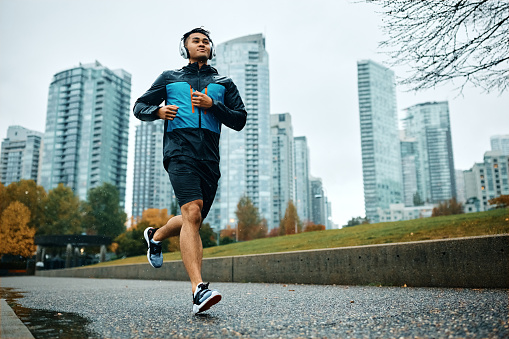 Low angle view of motivated athletic man running during rainy day. Copy space.