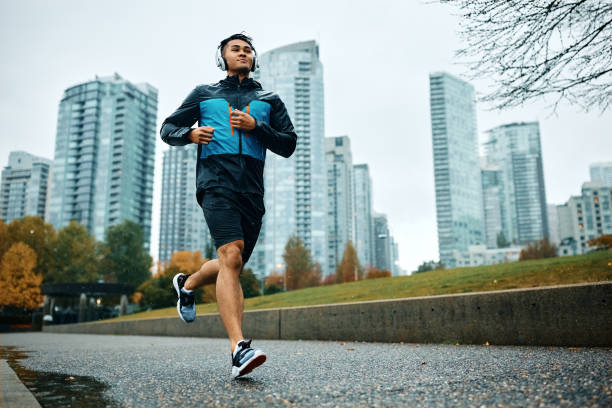 Below view of male athlete jogging in the rain. Low angle view of motivated athletic man running during rainy day. Copy space. asian man headphones stock pictures, royalty-free photos & images