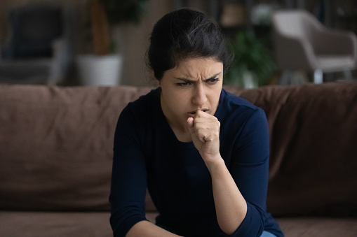 Unhealthy young Indian woman coughing, suffering from bronchitis disease or painful uncomfortable feelings in throat, caught cold, first flu grippe covid19 symptoms, immunity concept.
