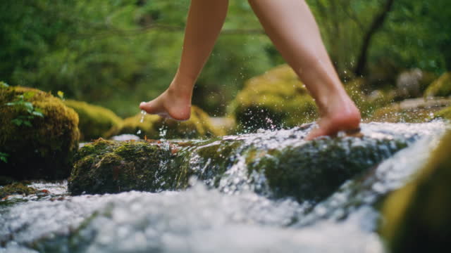 SLO MO Young woman crosses the stream barefoot