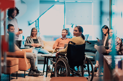 A businesswoman in a wheelchair having a business meeting with the team at a modern office. A group of young freelancers agree on new online business projects.
