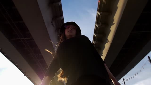 Expressive woman in black clothes dancing under the bridge in slow motion