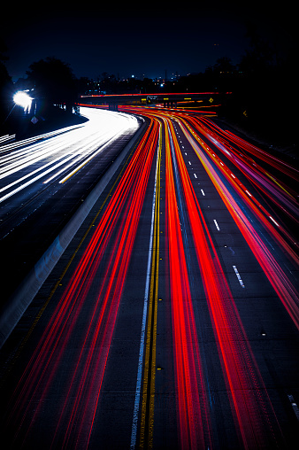 A wide highway with abstract bright traffic light trails at night, vertical background