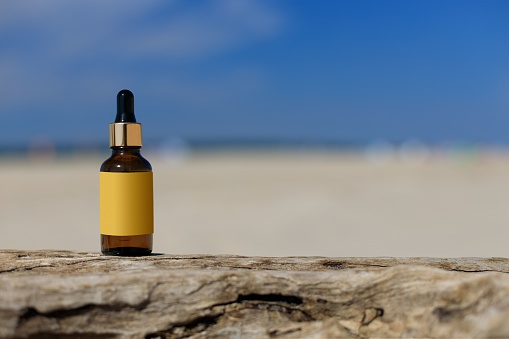 Cosmetic bottle against a blurred beach. Summer light, positive atmasphere. Mock-up for a cosmetic product. Copy space.