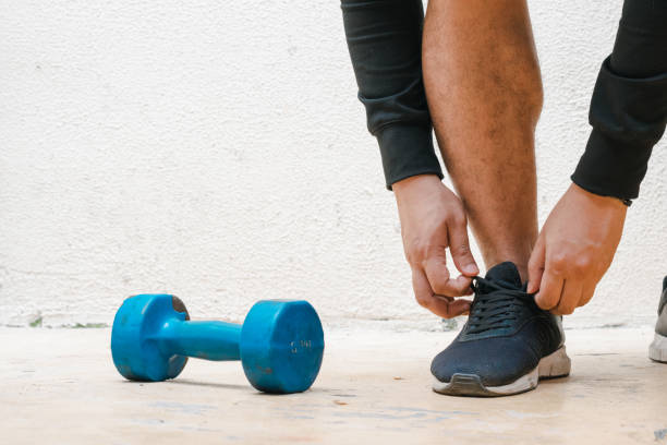 istock Man tying his shoe standing next to blue dumbbell 1442680675