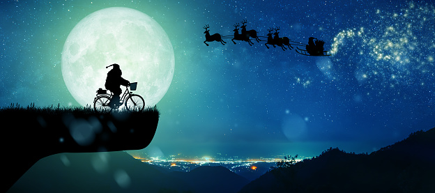 Silhouette of Santa Claus get a move to ride on their reindeer over full moon at night Christmas. Silhouette of Santa Claus on his bicycle to carry a gift under the Milky Way background.