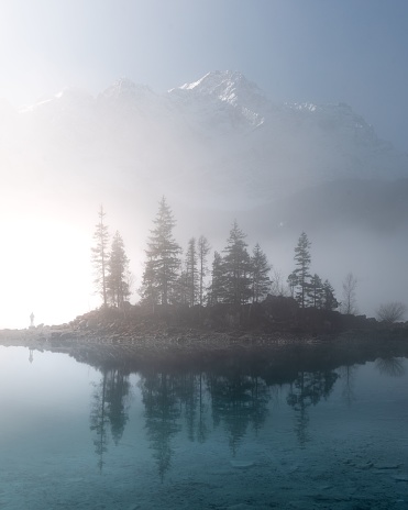 A mesmerizing foggy vertical view of an island on the Eibsee lake with trees reflecting on the water