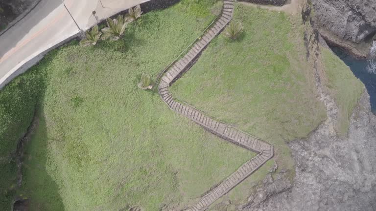 Drone footage of a rocky shore with a narrow staircase between the road and ocean in Philippines