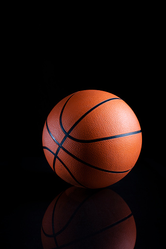 A vertical closeup shot of a brown basketball ball with black stripes on a black background with a reflection